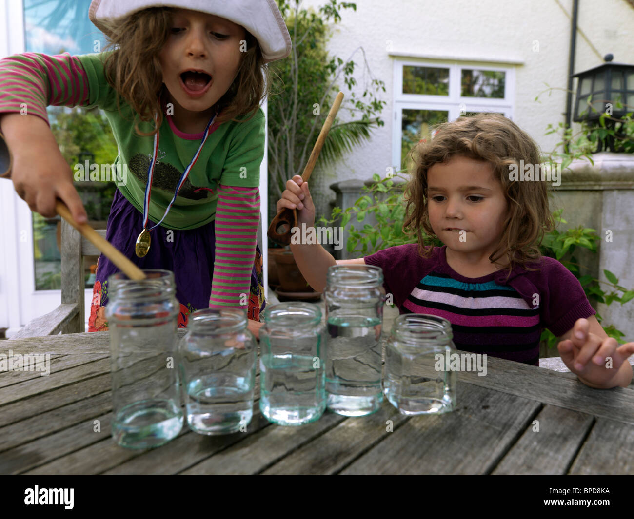 Girls Making Music Using Glass Jars Full Of Water And Hitting Them With Wooden Spoons Stock Photo