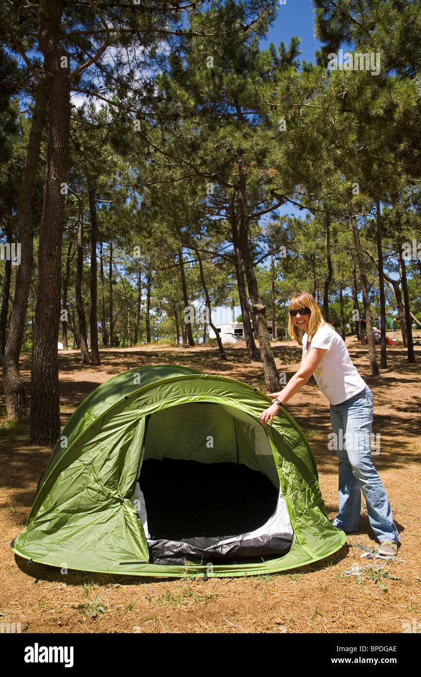 A blonde woman enjoys camping as she pitches her green tent. Stock Photo