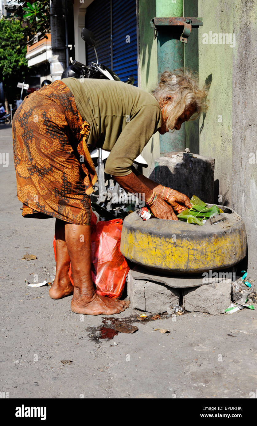 elderly local woman scavenging for food in rubbish bin in a kuta street bali Stock Photo