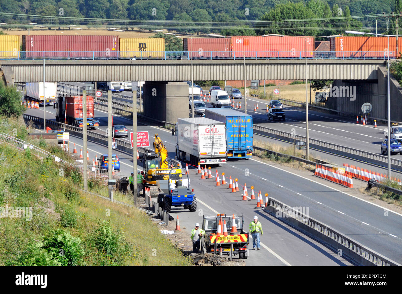 Transport by freight train loaded with shipping containers on bridge above trucks road works on M25 motorway at junction 28 Brentwood Essex England UK Stock Photo