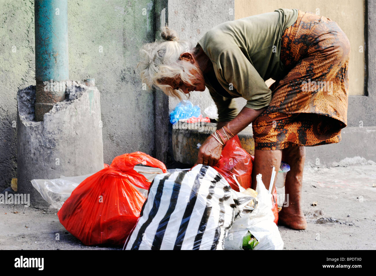 elderly local woman scavenging for food in rubbish bin in a kuta street bali Stock Photo