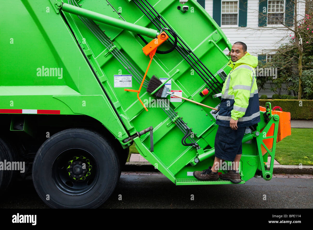 Pacific Islander man riding on garbage truck Stock Photo