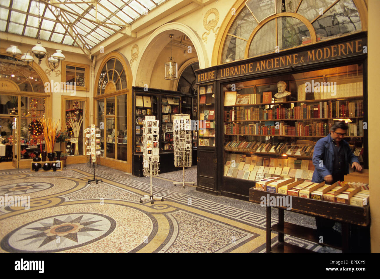 France, Paris, 2nd arrondissement, Gallerie Vivienne, a covered shopping gallery or 'passage couvert', bookseller arranges books Stock Photo