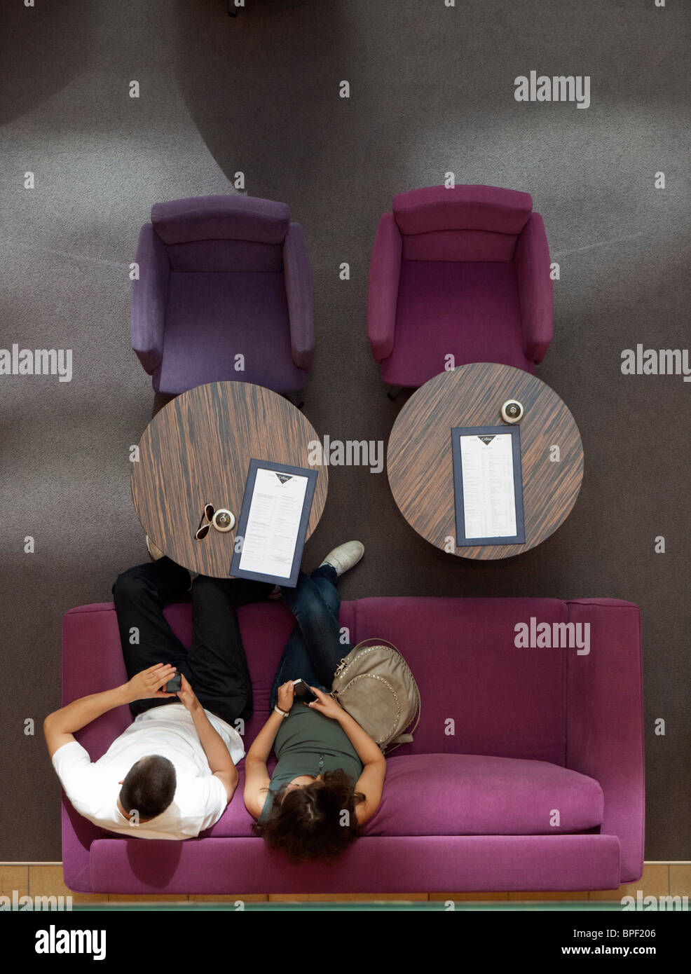 Couple using mobile phones on colorful sofa inside upmarket shopping mall on Friedrichstrasse in Berlin Germany Stock Photo