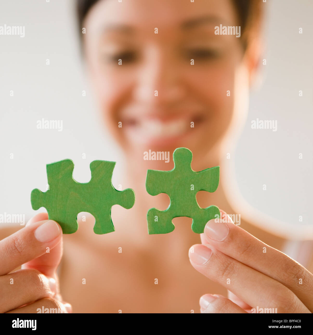 Mixed race woman holding green jigsaw puzzle pieces Stock Photo