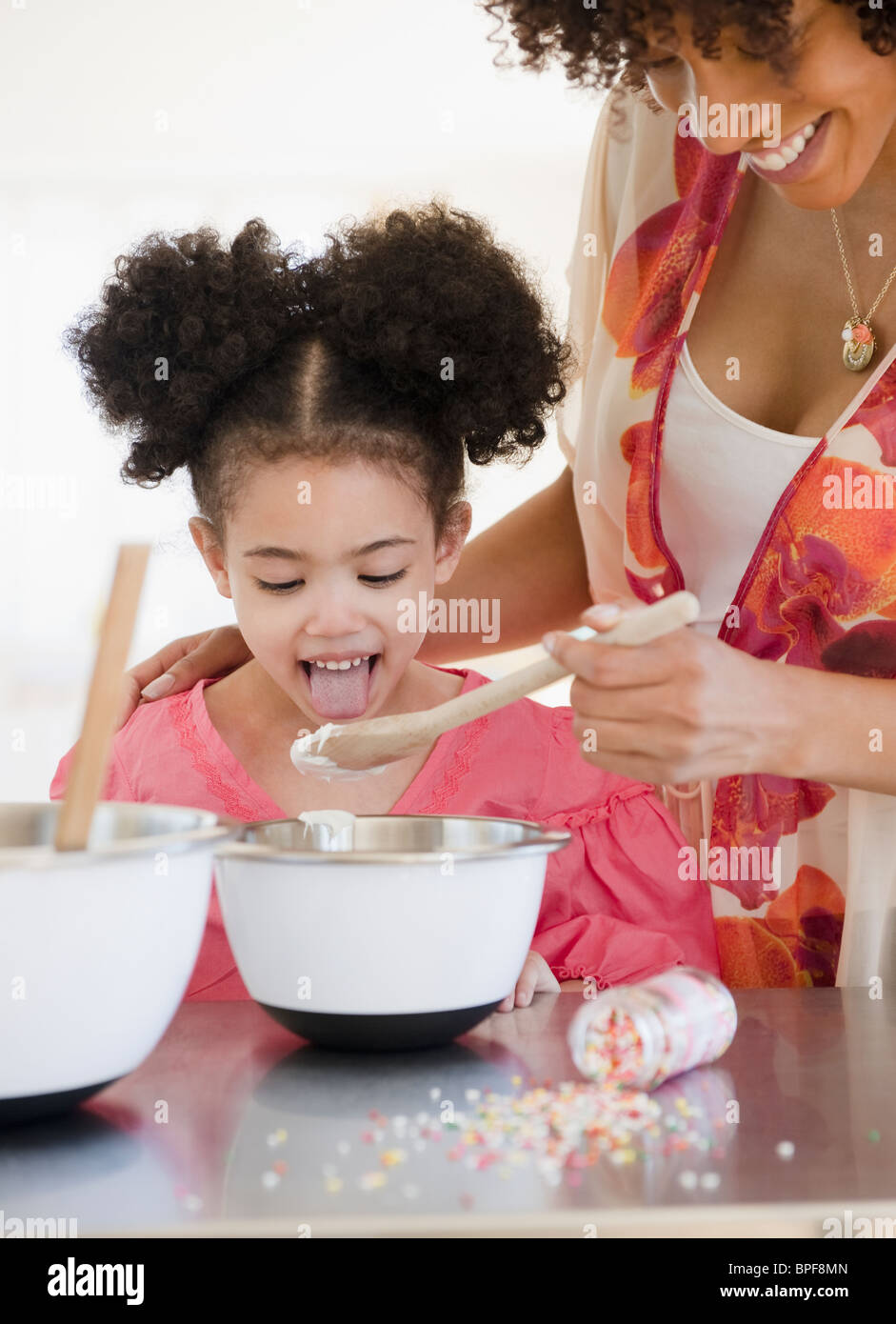 Mother feeding daughter from mixing bowl Stock Photo