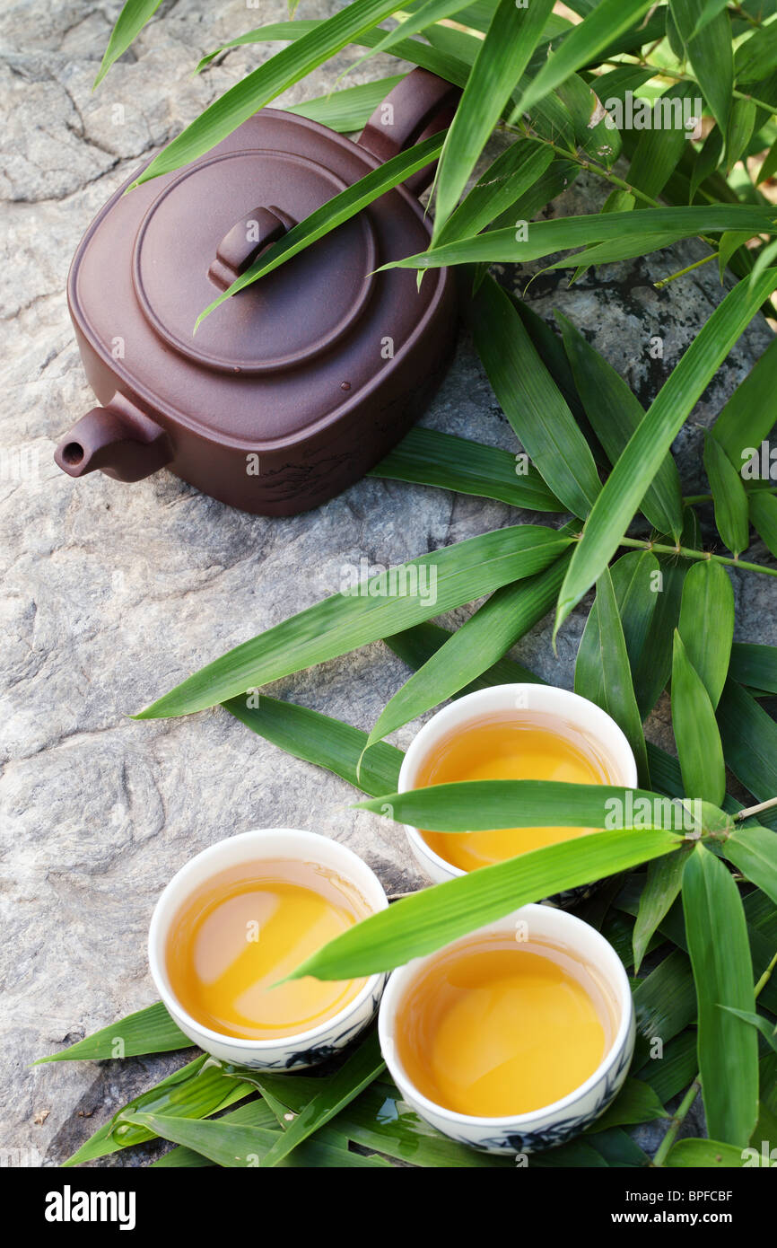 Teapot and cups on stone with bamboo leaves. Stock Photo