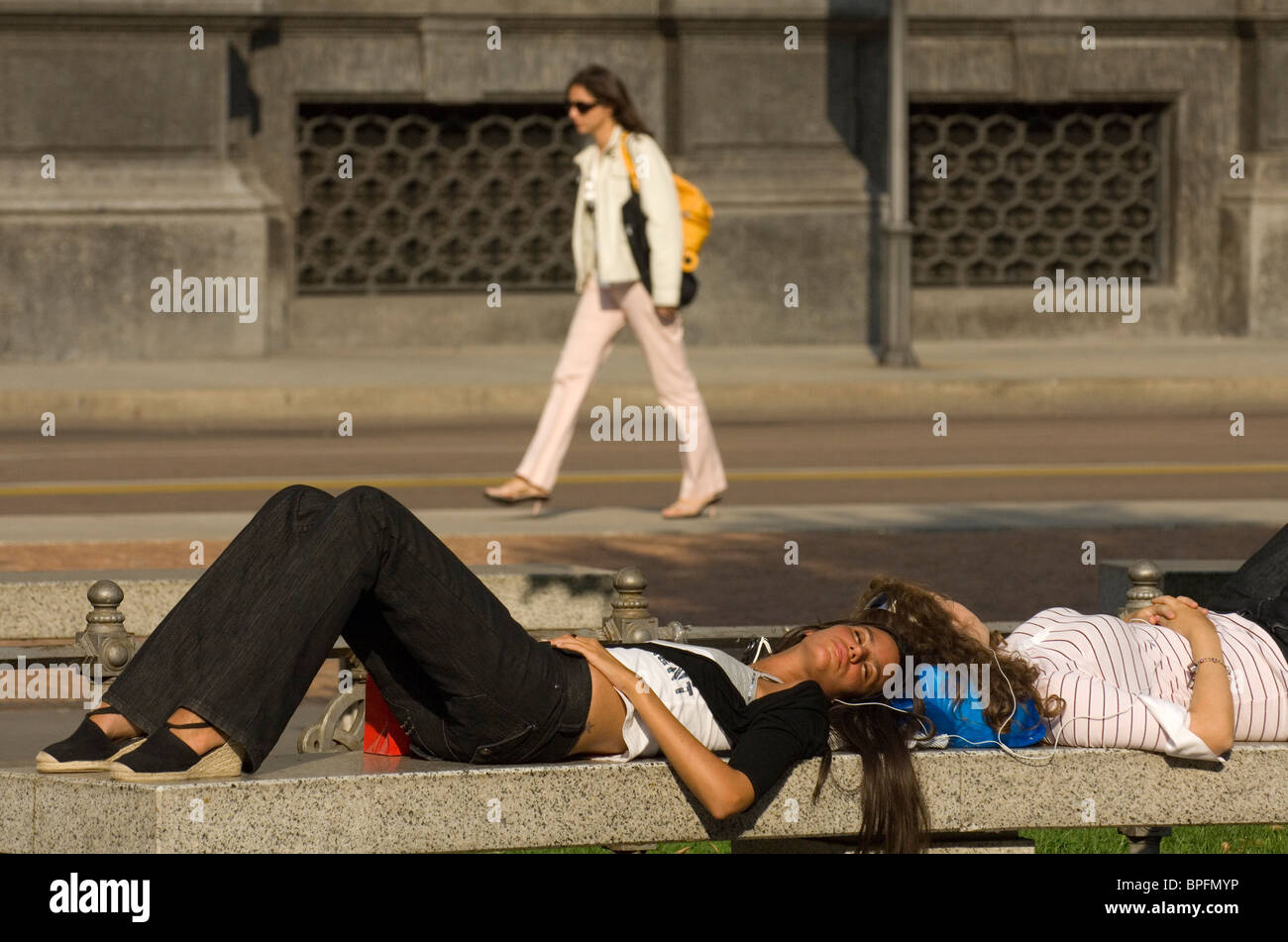 Young girls relaxing on a bench and listening to music, Milan, Italy Stock Photo