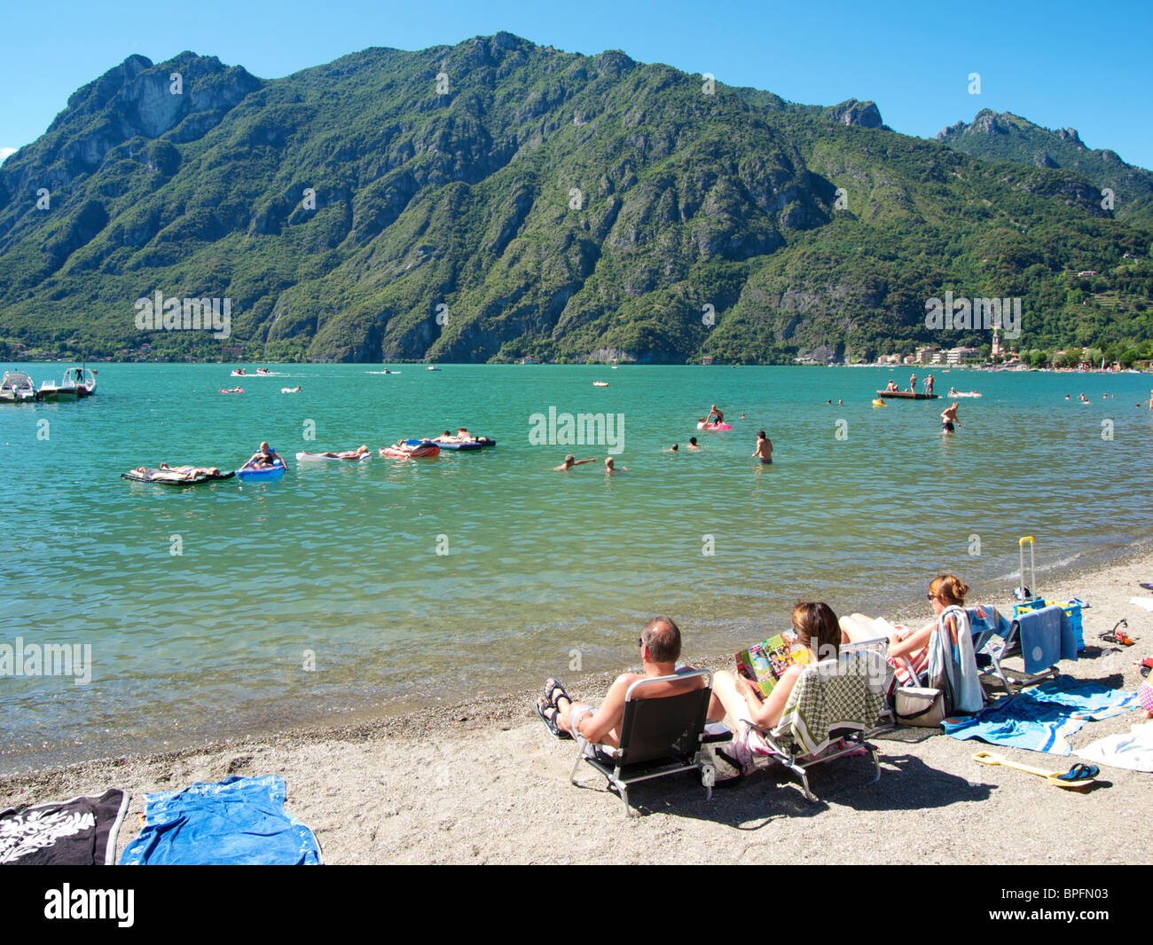 People sitting on the narrow beach and swimming at Porlezza, Lake Lugano, Italy Stock Photo