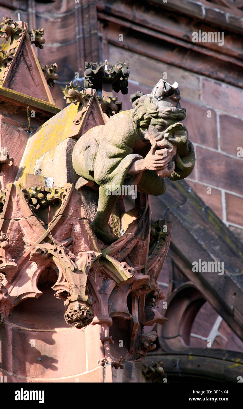 Gargoyle in the form of a seated man holding his nose and vomiting, on Freiburg Münster, Freiburg im Breisgau, Germany Stock Photo