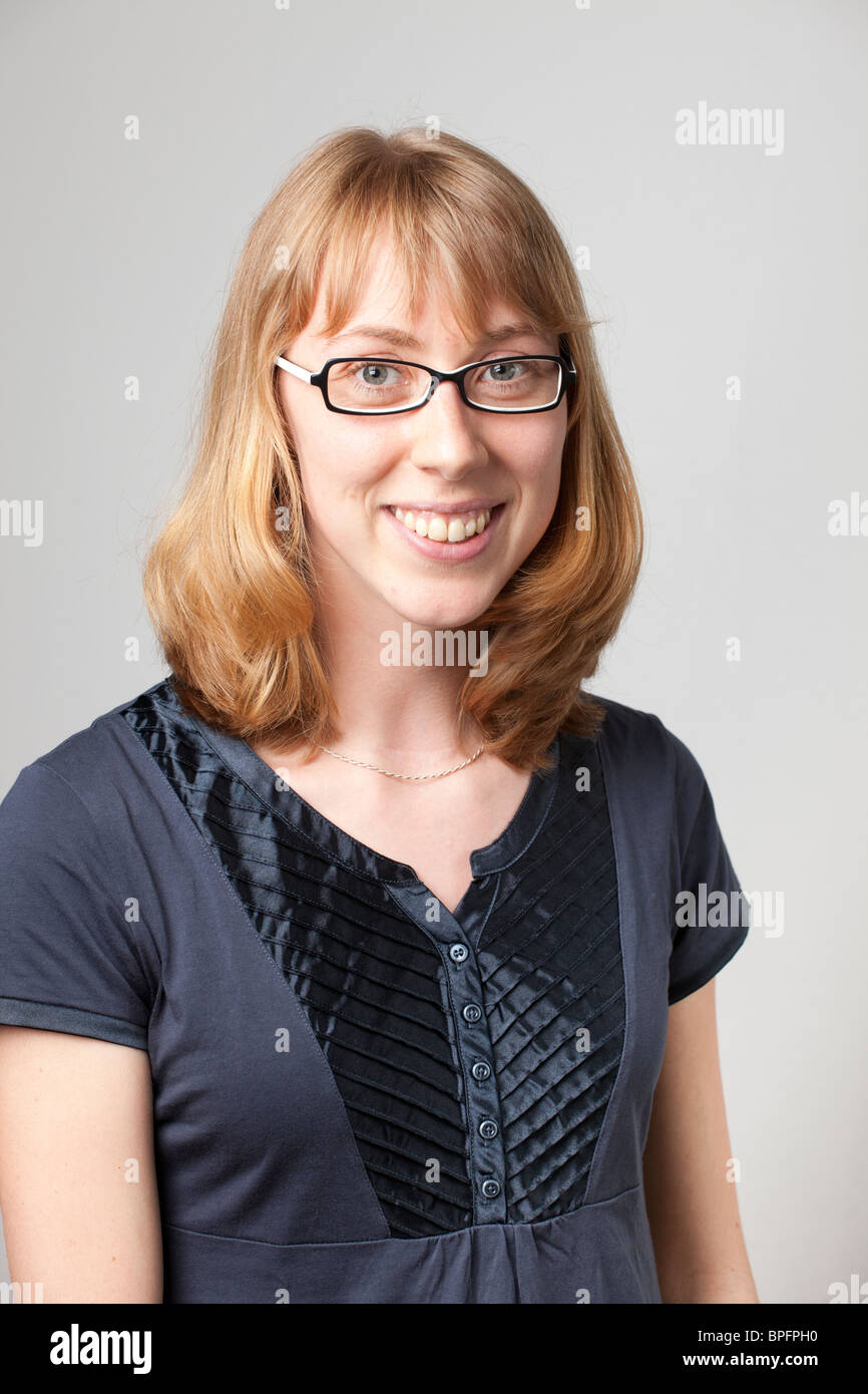 Smiling woman with glasses and short blonde hair, wearing a navy blue top, looking at the camera in a studio shot. Stock Photo