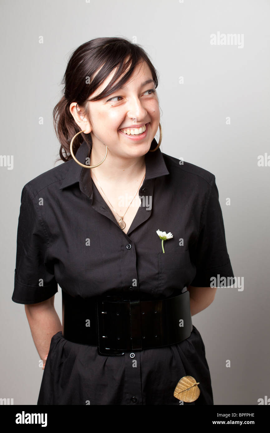 Smiling woman in a black dress with a white flower pin and large hoop earrings, looking off-camera. Stock Photo