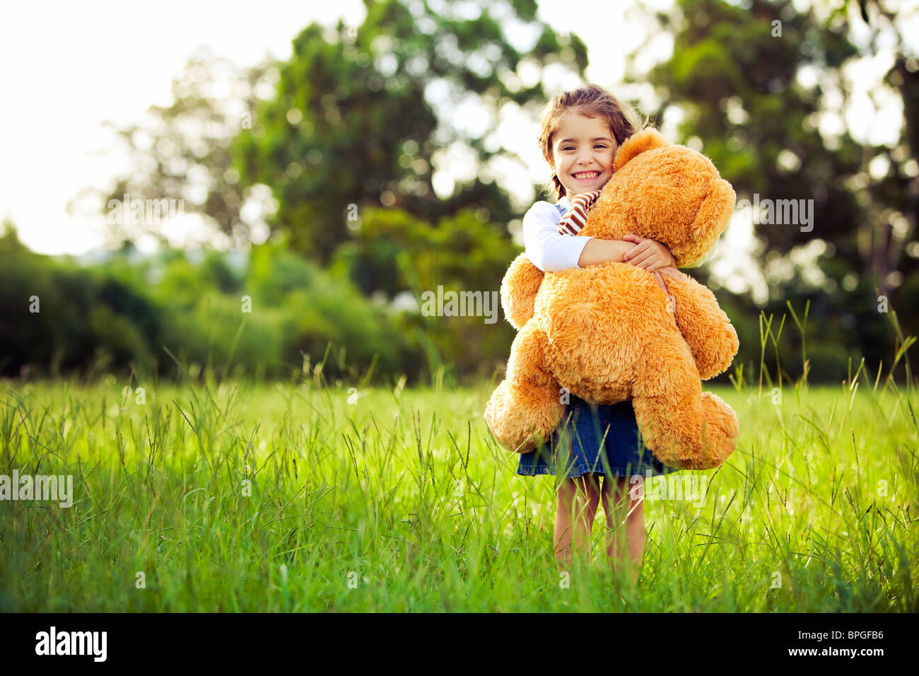 Little cute girl standing in the grass holding large teddy bear Stock ...