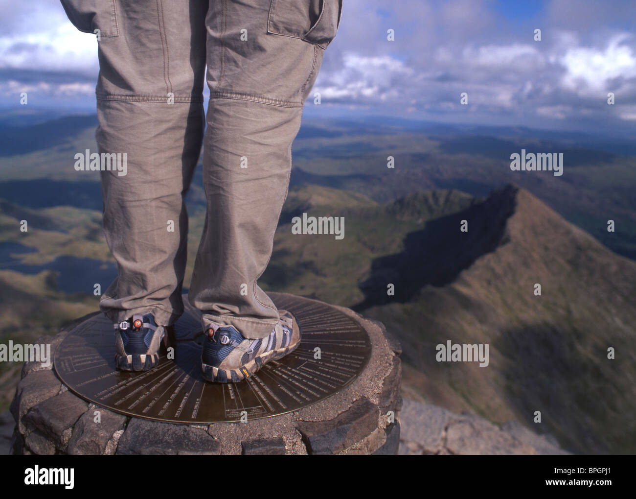 Walker standing on trig point on summit of Snowdon (Yr Wyddfa) near Llanberis Gwynedd Snowdonia National Park North Wales UK Stock Photo