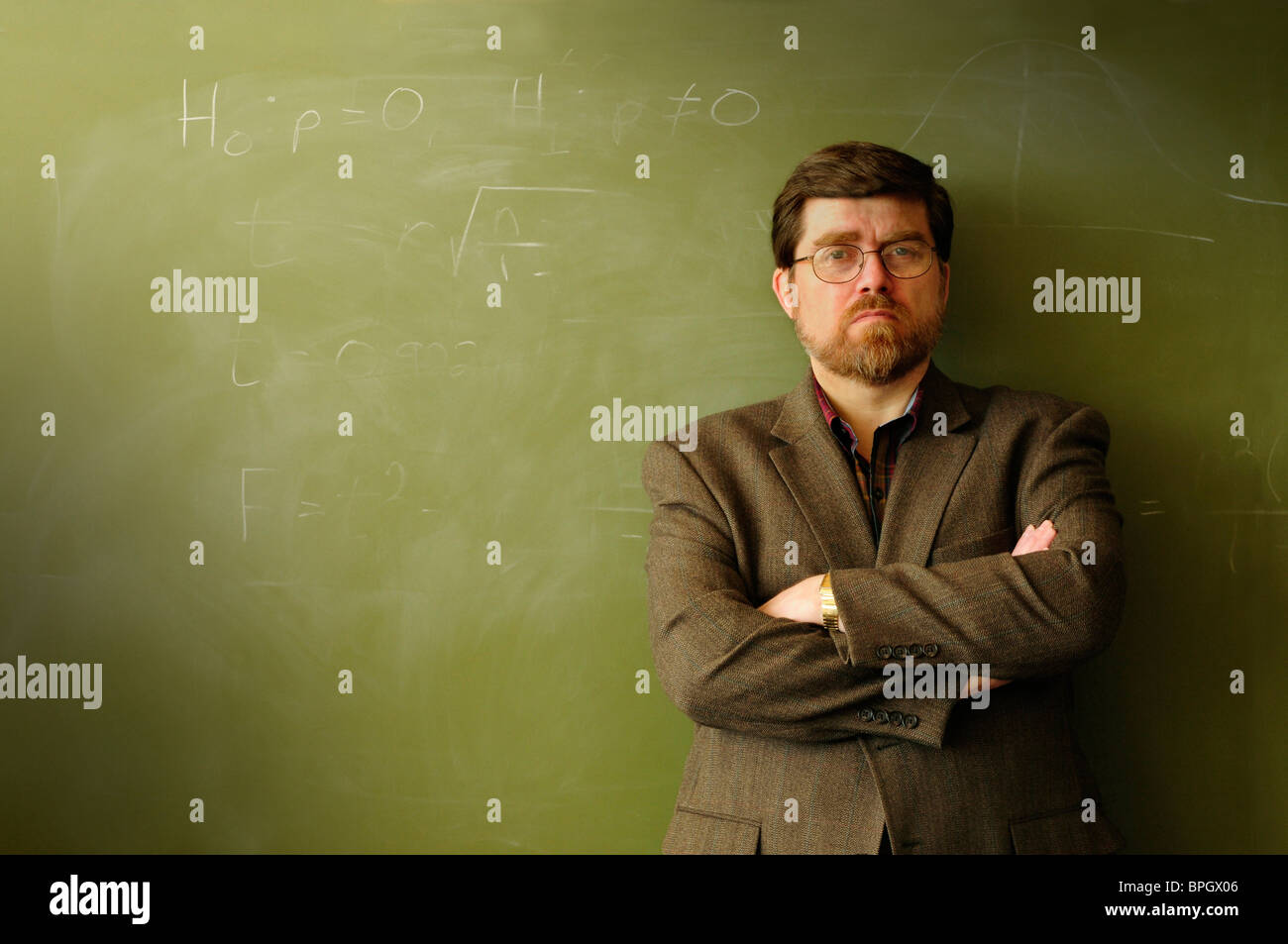 Math professor or teacher standing in front of a green chalkboard, possibly annoyed or determined. Stock Photo