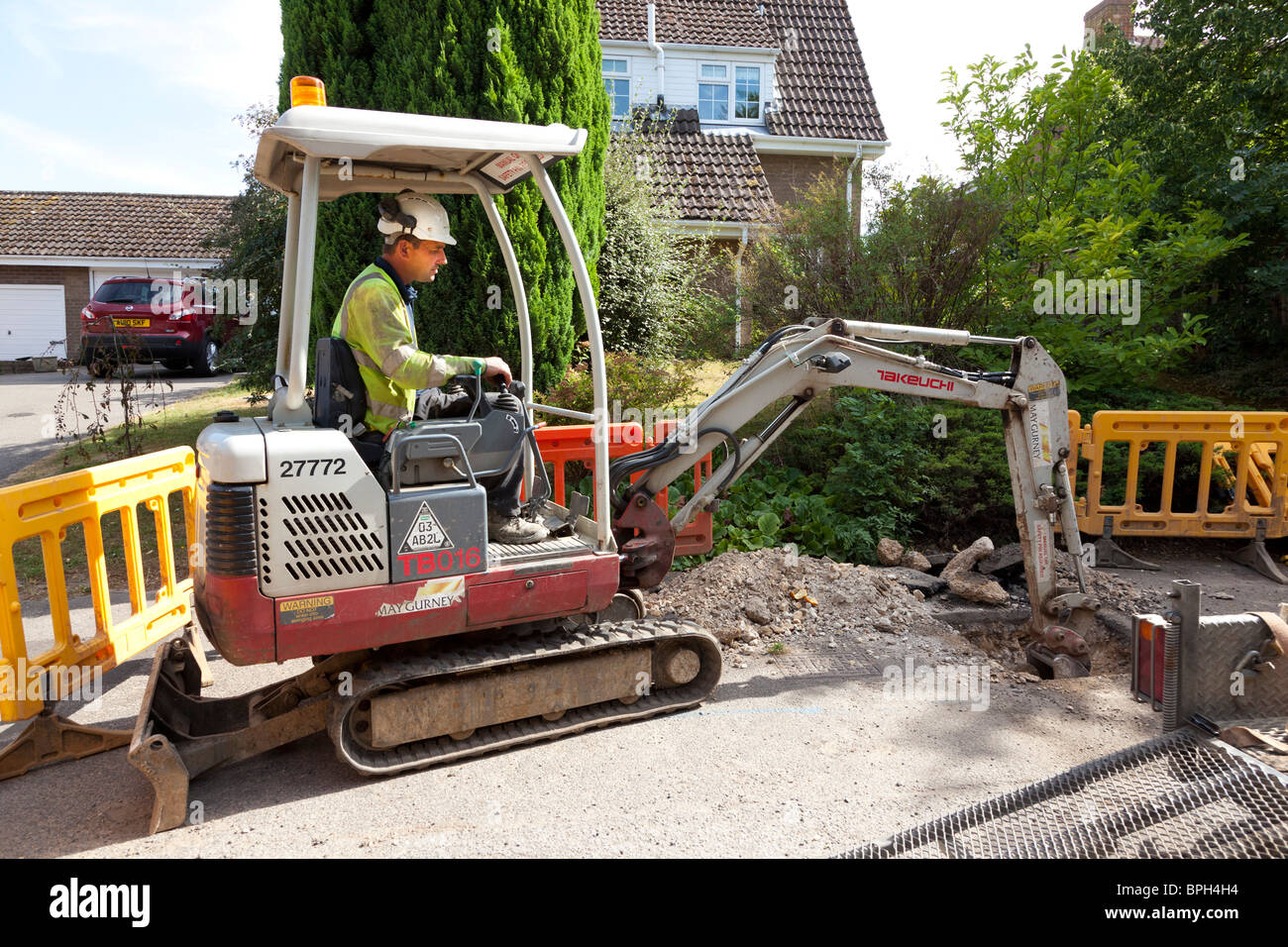 workers using a mini excavator to dig a trench in the road Stock Photo