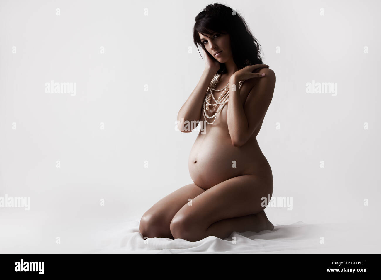 Young nude pregnant woman sitting on the ground isolated Stock Photo