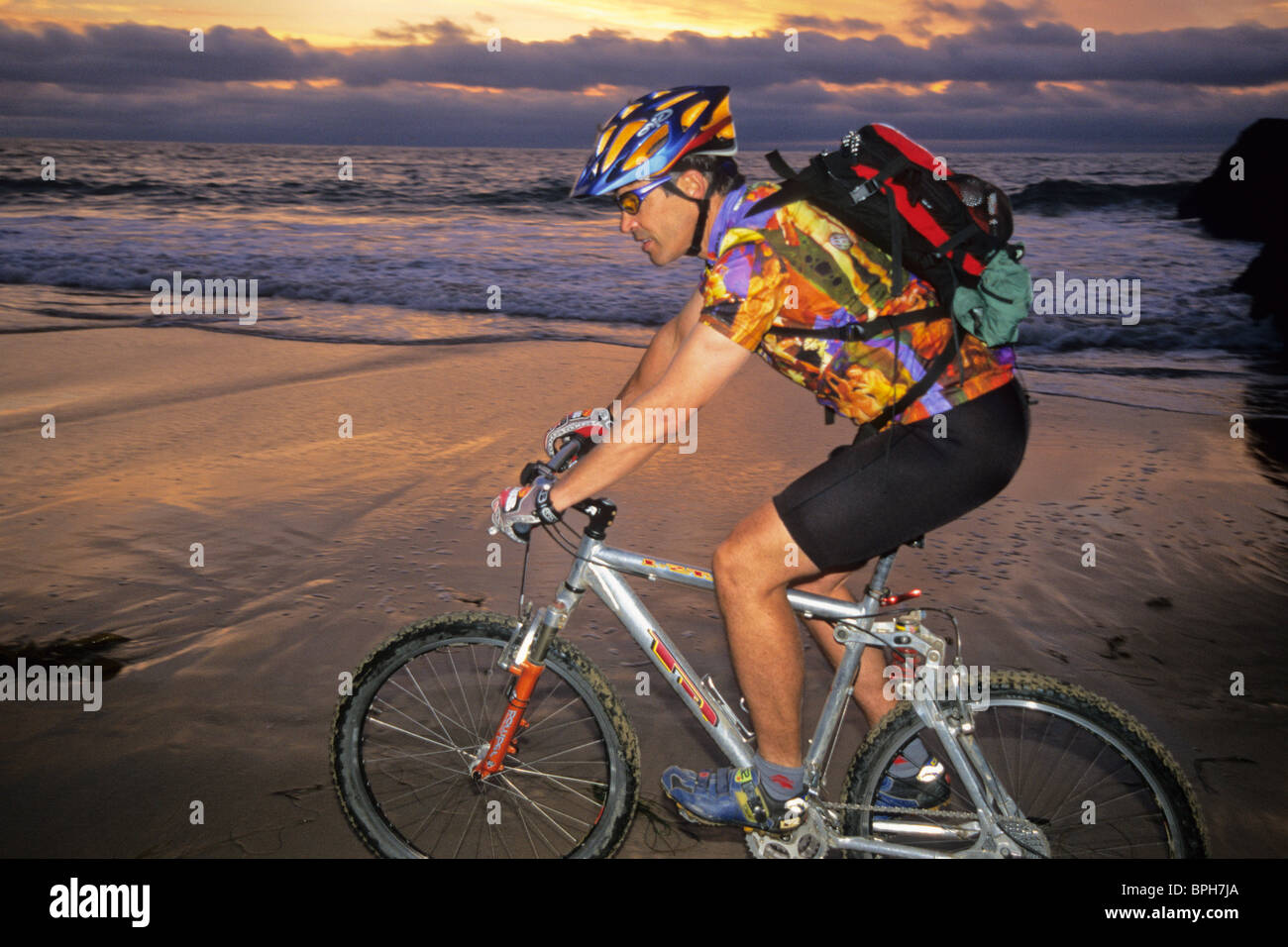 Man riding bike on beach at sunset Stock Photo Alamy