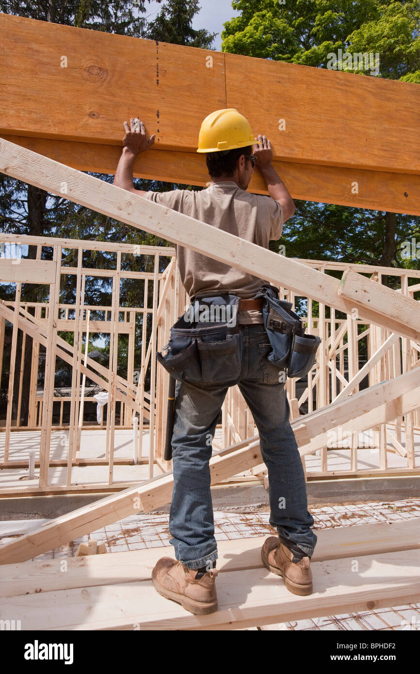 Carpenter lifting a laminated beam at a construction site Stock Photo