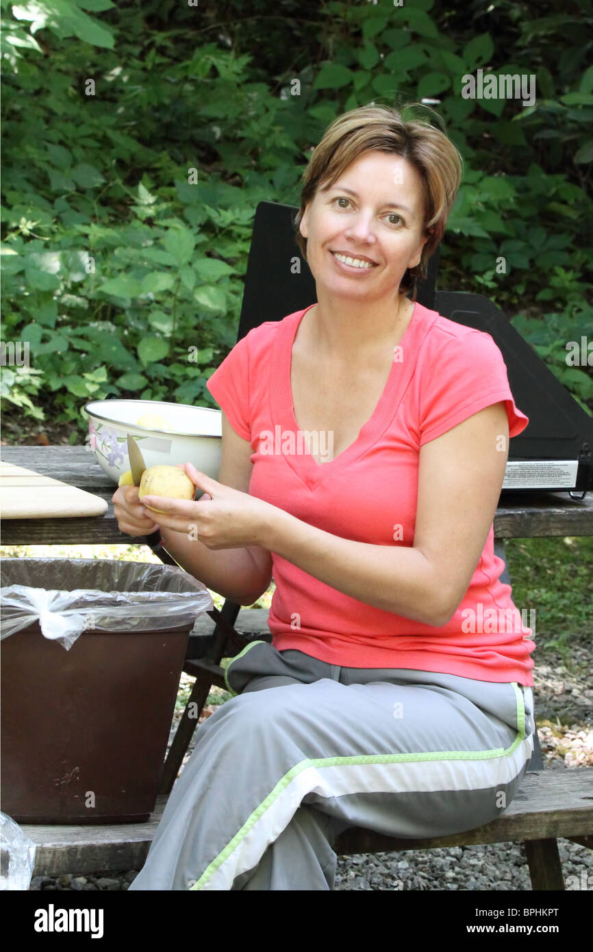 Woman is peeling potato for breakfast or lunch outdoor in camping Stock Photo