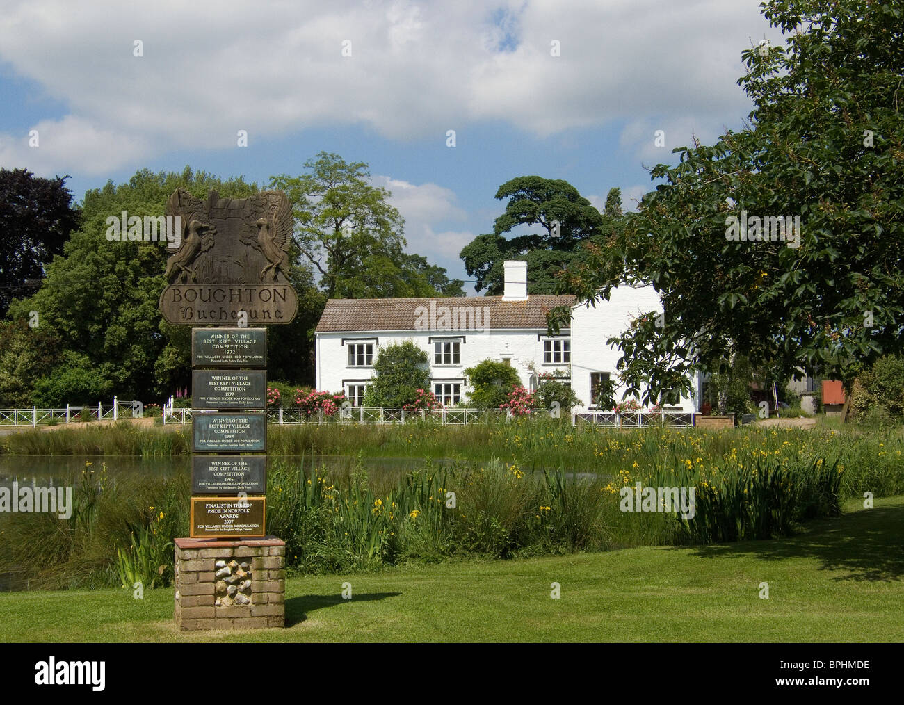 Boughton village sign in Norfolk, England looking across the duck pond to Manor Farmhouse in the background on a sunny June day Stock Photo