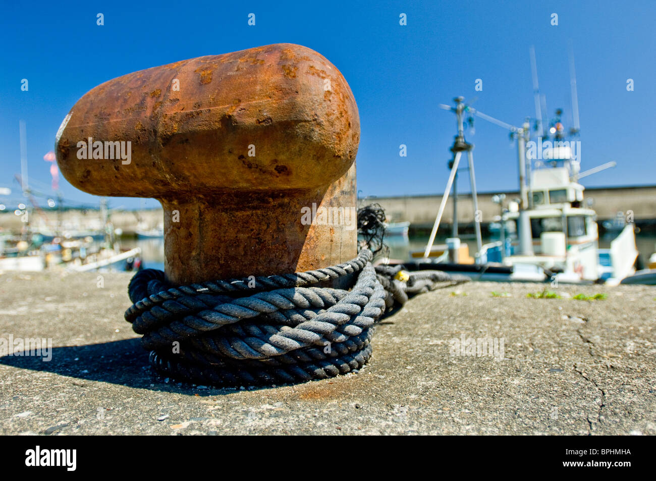 Rusted bollard with boats in port and a blue sky in the background Stock Photo