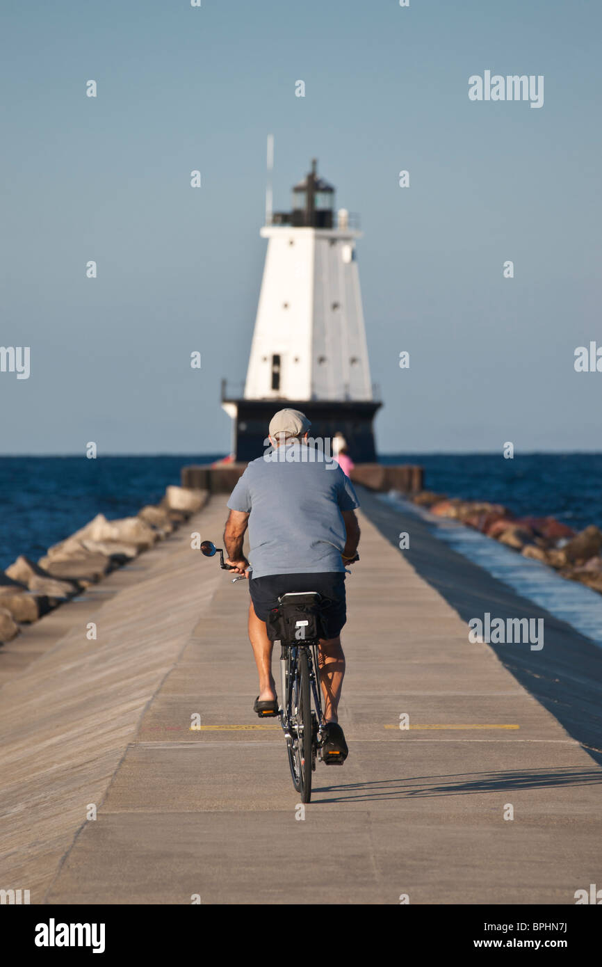 A bicyclist riding a bike on a breakwall leading into the Ludington North Breakwater Light lighthouse hi-res Stock Photo
