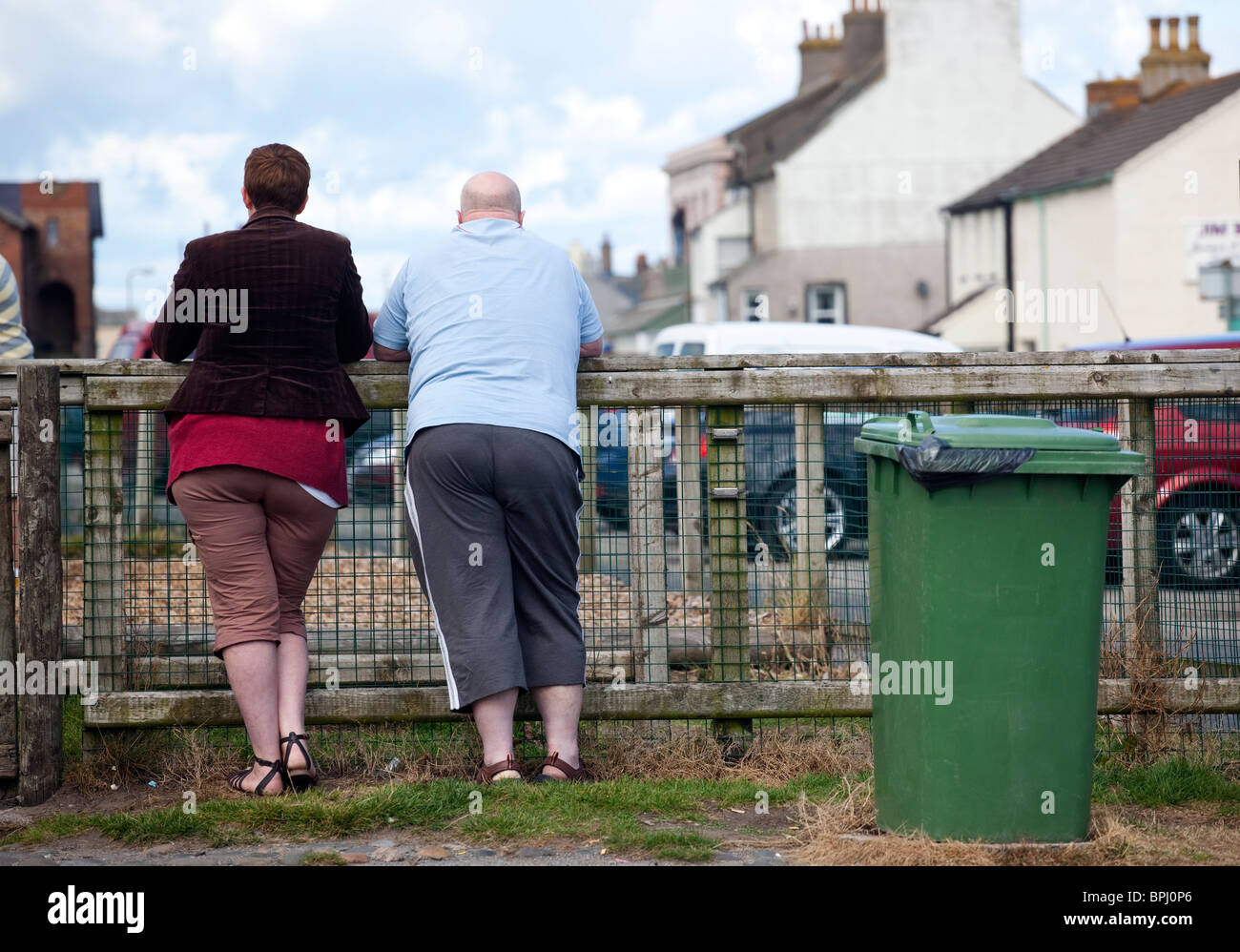 Two overweight people leaning on a fence in the West Cumbria village of Allonby. Stock Photo