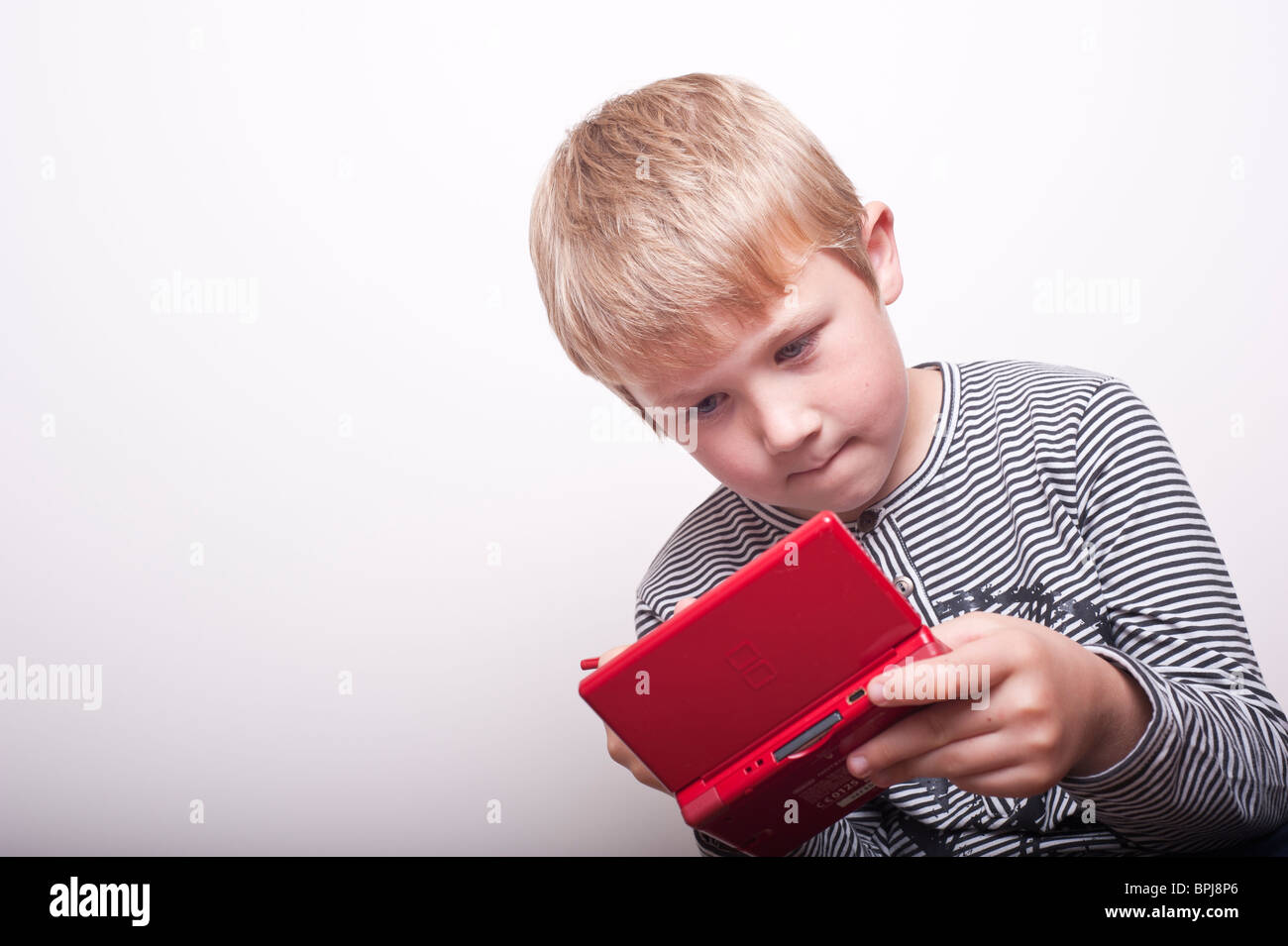 A MODEL RELEASED picture of a 6 year old boy playing with a Nintendo DS handheld games console in the studio Stock Photo