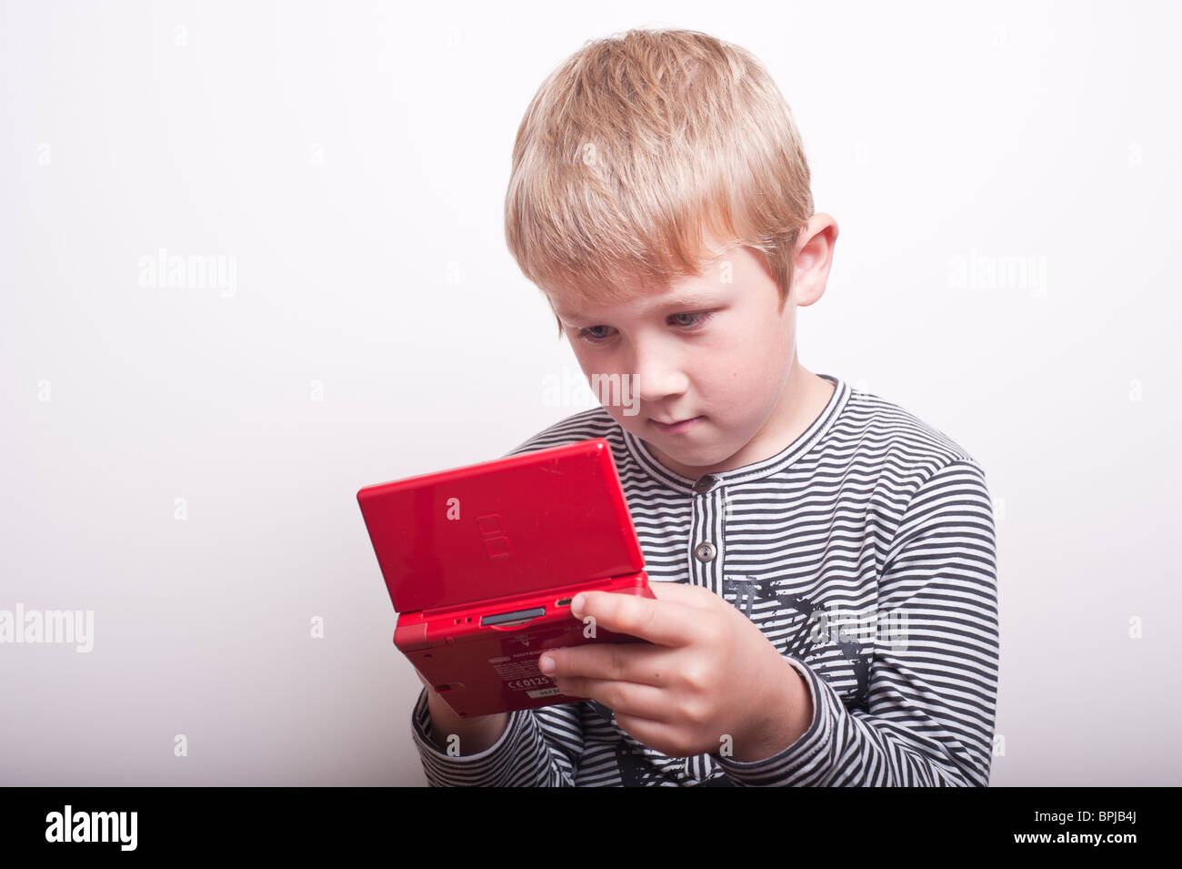 A MODEL RELEASED picture of a 6 year old boy playing with a Nintendo DS handheld games console in the studio Stock Photo