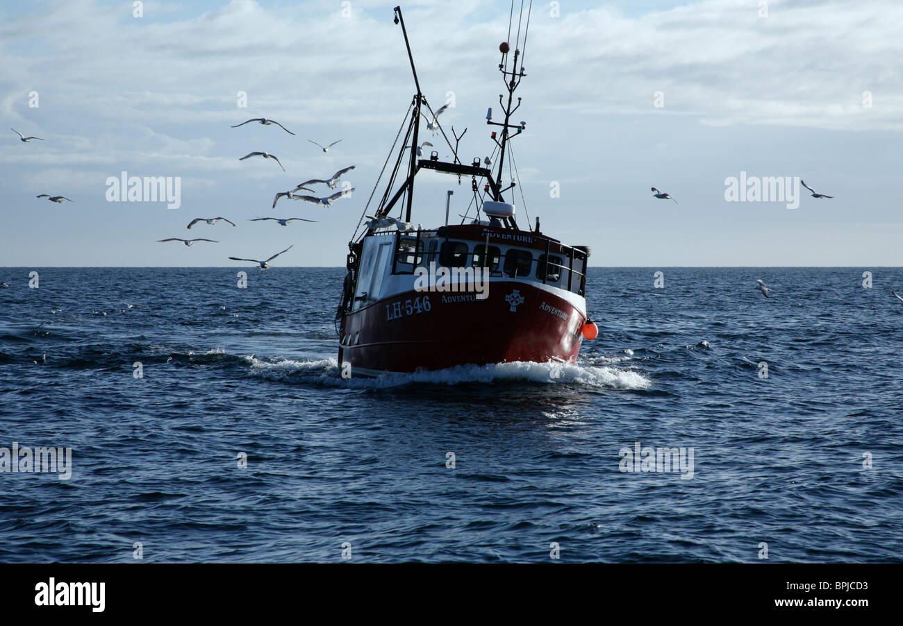 A rolling fishing boat making for its home port with its catch pursued by seagulls Stock Photo