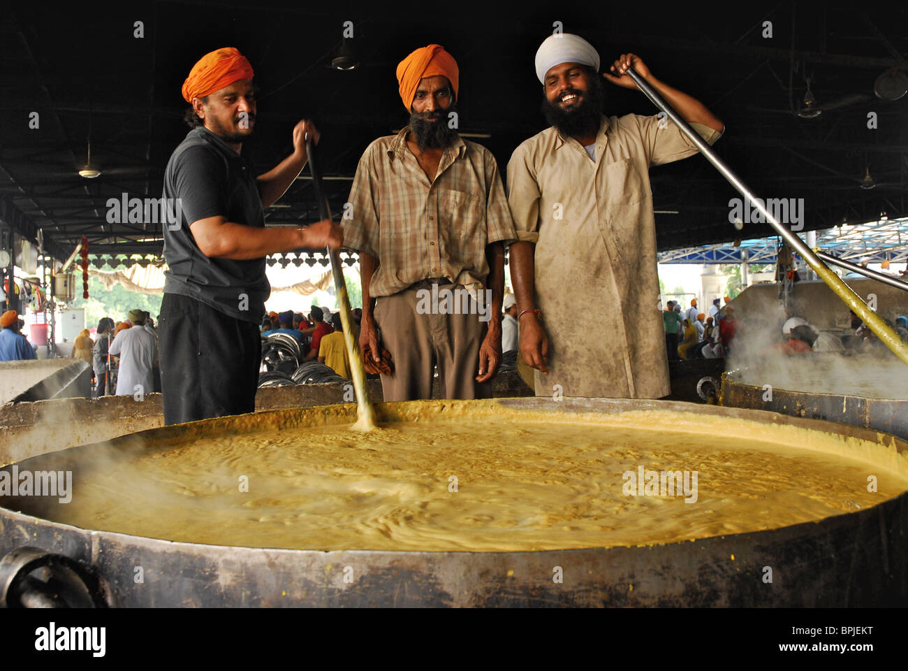 A cook in a Sikh kitchen cooking in an extremely large pot.