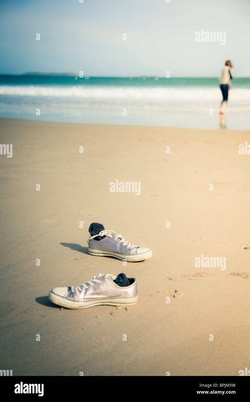 Shoes left on a sandy beach. Owner can be seen in distance entering the