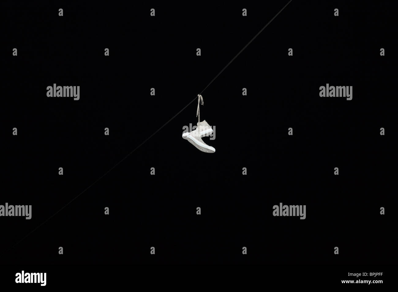 White sneakers shoes hanging by their shoelaces on a wire at night Stock Photo