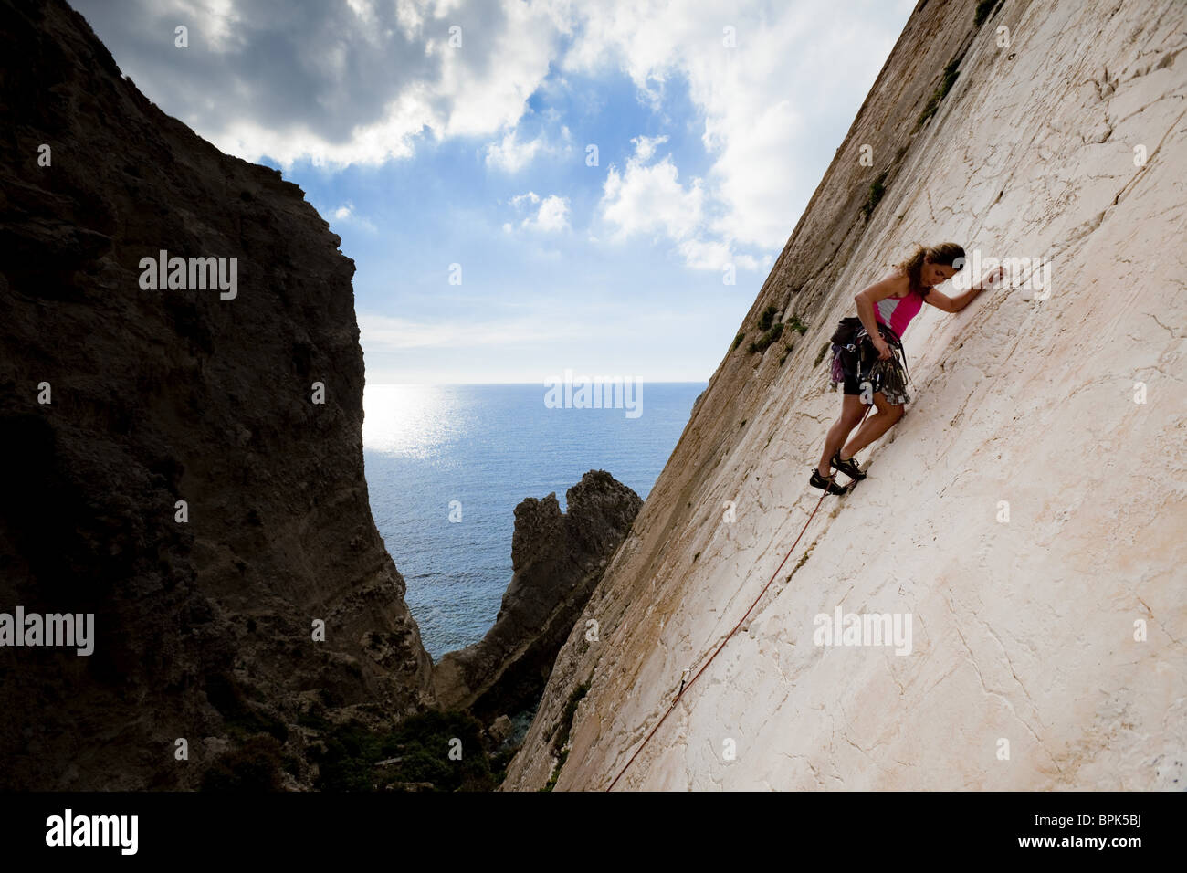 A young woman, a climber, a sportclimber, freeclimber, climbing at Ix-Xaqqa rock face, Malta, She protects with nuts and wires, Stock Photo