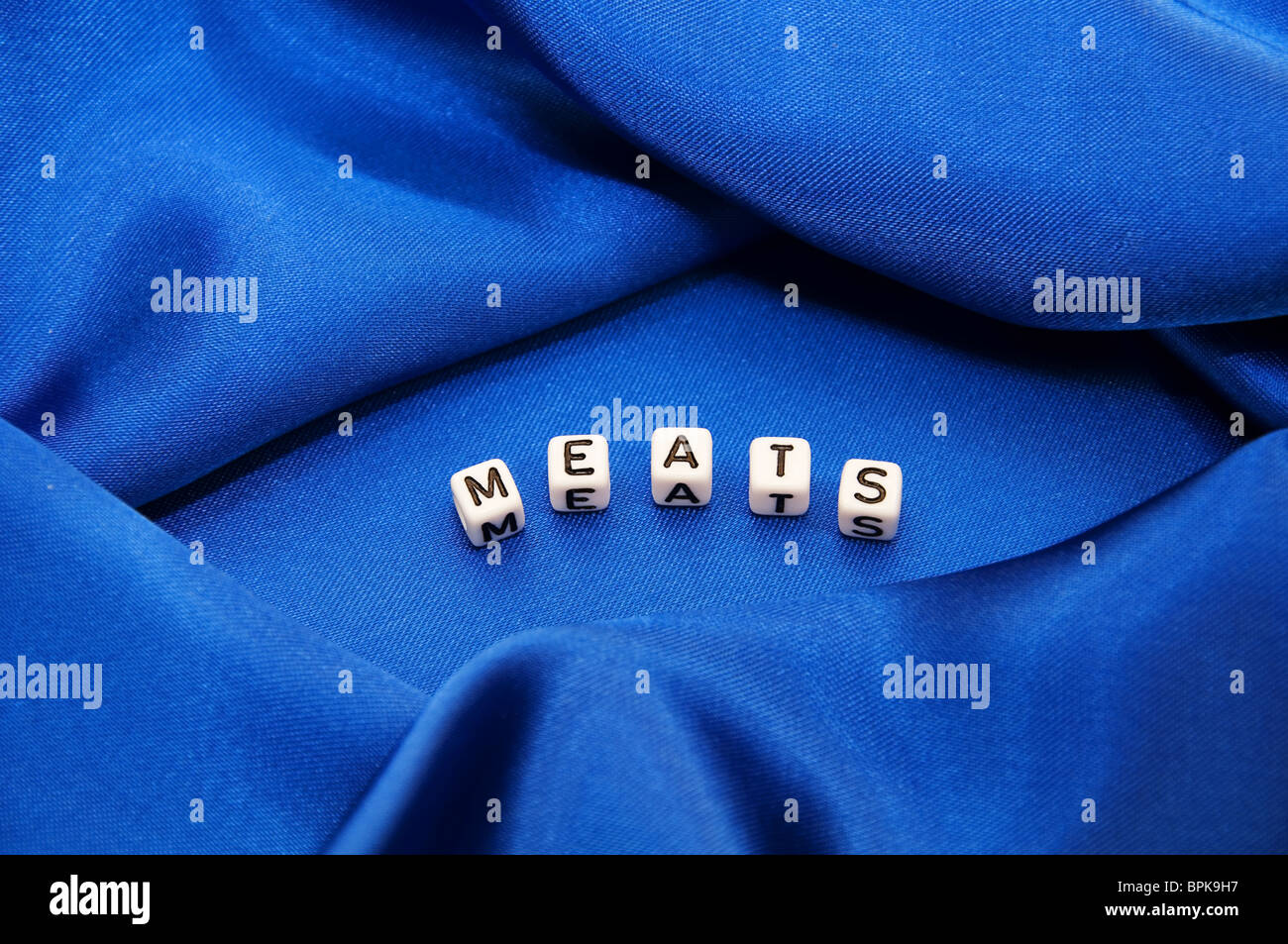 Royal blue satin background with rich folds and wrinkles for texture is the word Meats in black and white cube lettering series. Stock Photo