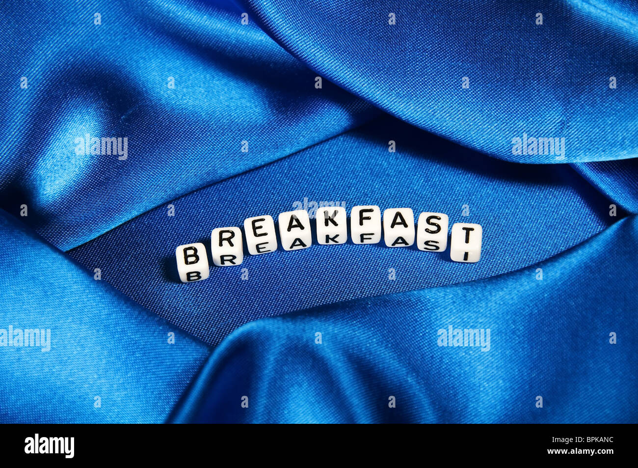 Royal blue satin background with rich folds and wrinkles for texture is the word Breakfast in cube lettering series. Stock Photo