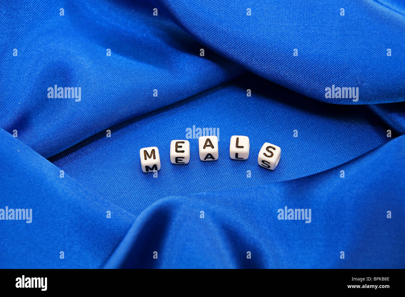 Photo is royal blue satin fabric with folds and texture and wrinkles with the word Meals written in cube lettering series Stock Photo