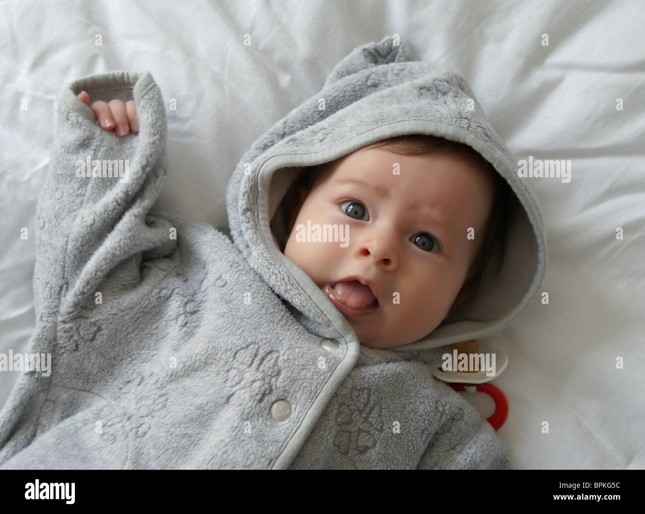 Baby with gray hood coat, dropped the red soother, on the white blanket Stock Photo