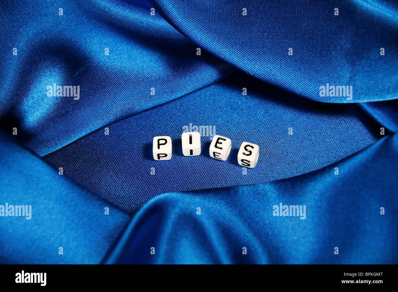 Royal blue satin background with rich folds and wrinkles for texture is the word Pies in black and white cube lettering series. Stock Photo