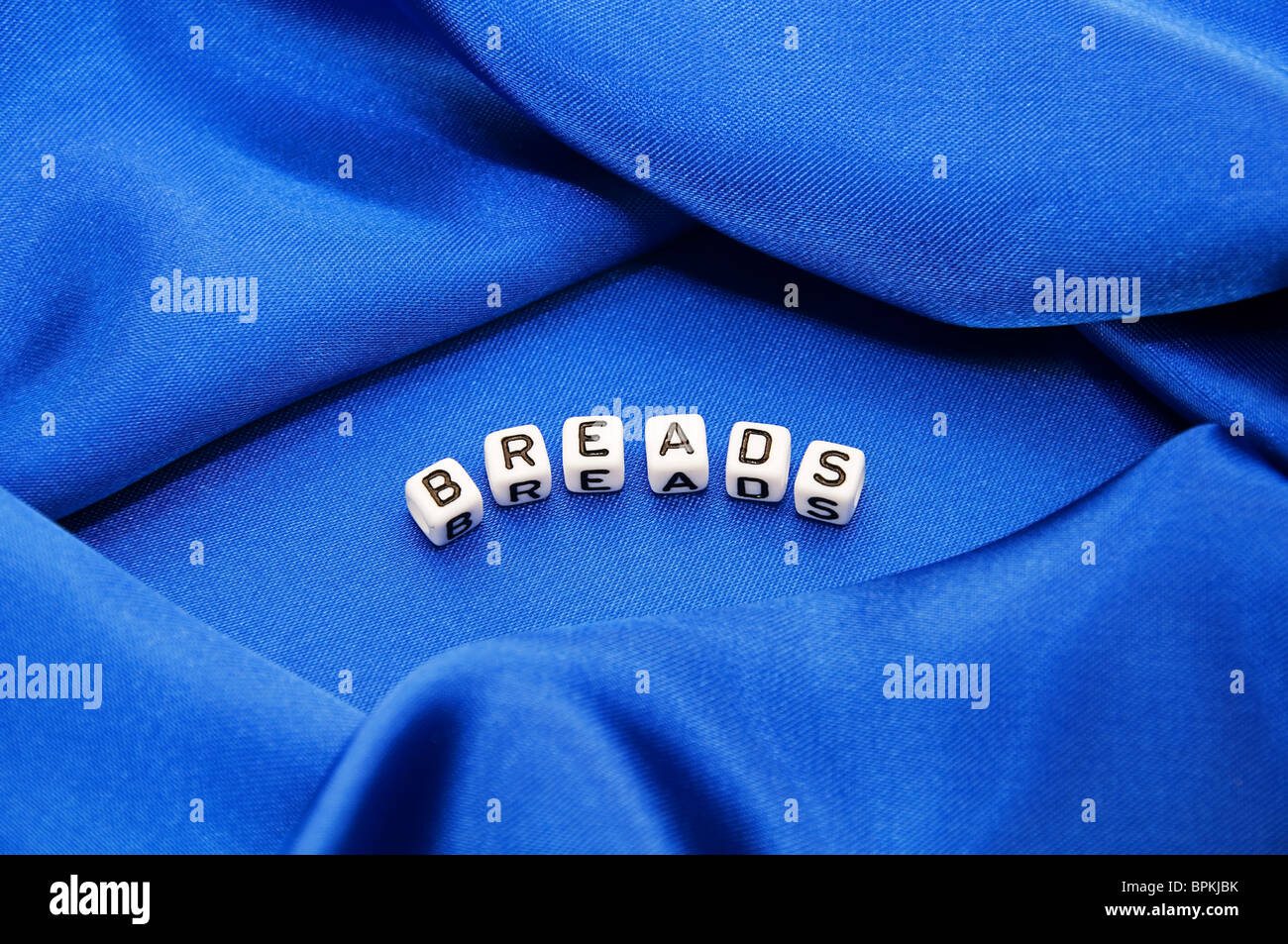 Royal blue satin background with rich folds and wrinkles for texture is the word breads in black and white cube lettering series Stock Photo