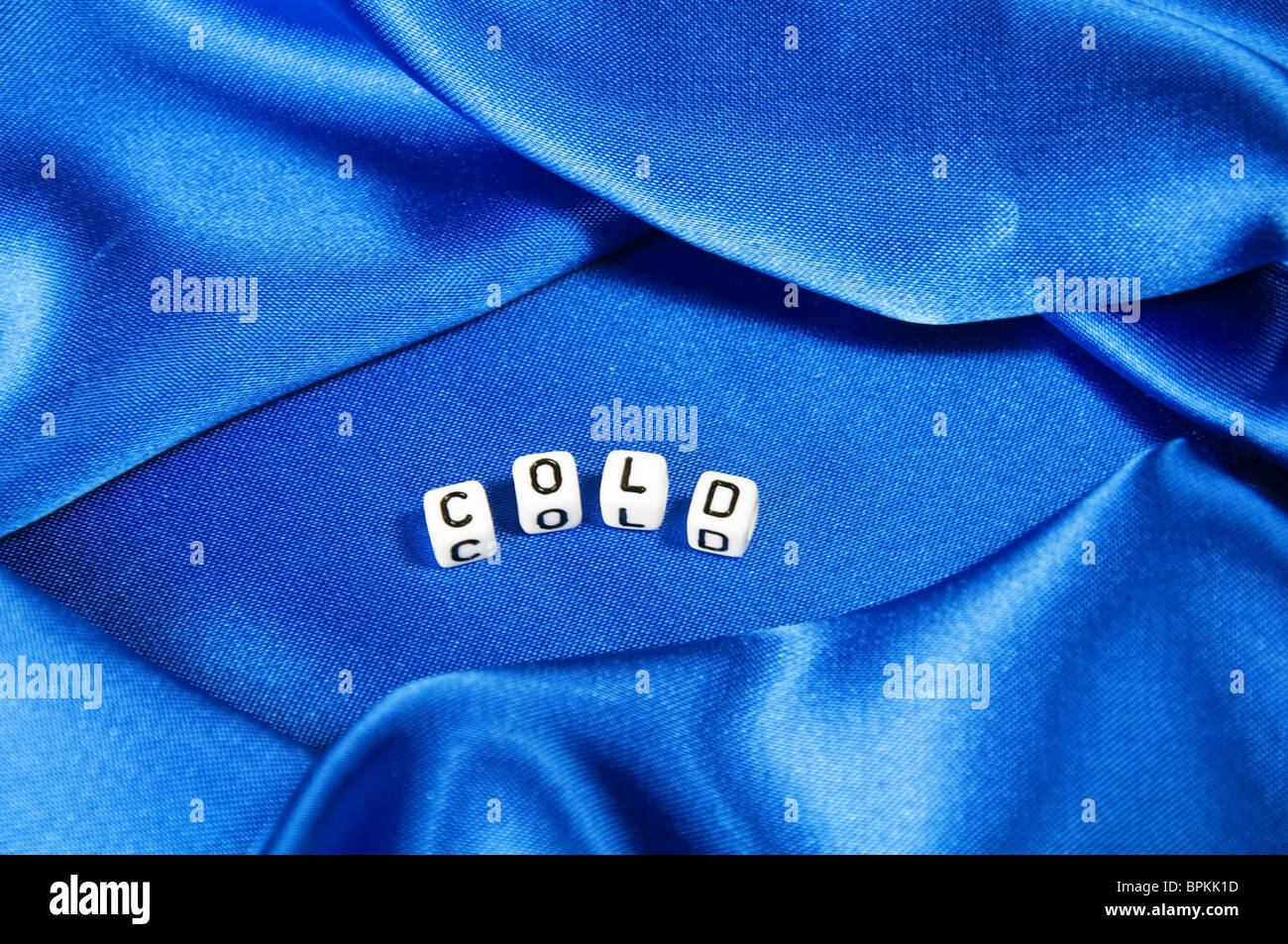 Royal blue satin background with rich folds and wrinkles for texture is the word cold in black and white cube lettering series. Stock Photo