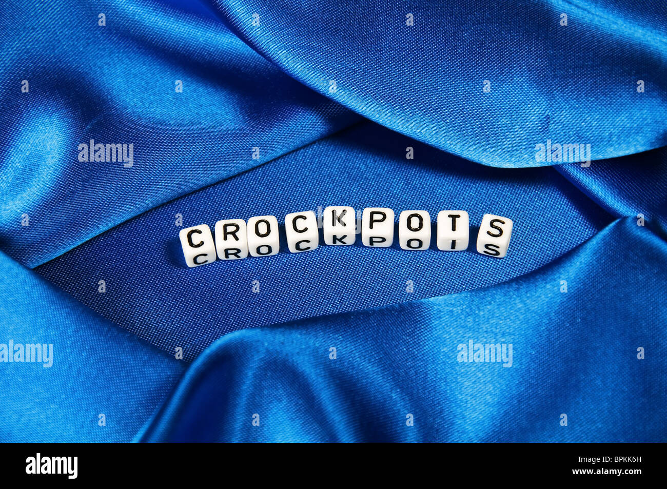 Royal blue satin background with rich folds and wrinkles for texture is the word crockpots in  cube lettering in series Stock Photo