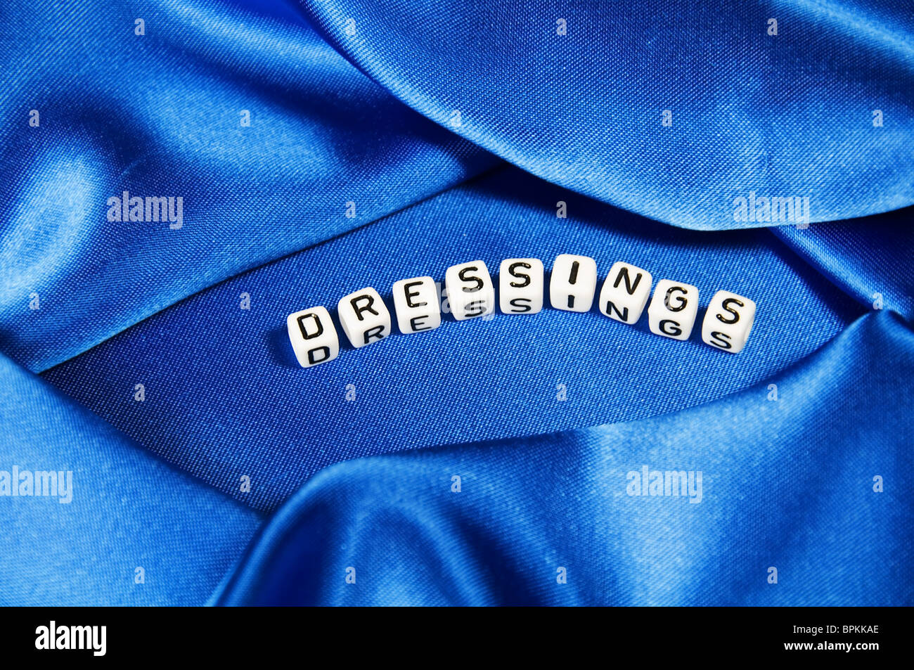 Royal blue satin background with rich folds and wrinkles for texture is the word dressings in cube lettering series Stock Photo