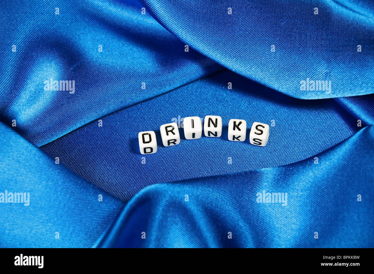 Royal blue satin background with rich folds and wrinkles for texture is the word drinks in black and white cube lettering series Stock Photo