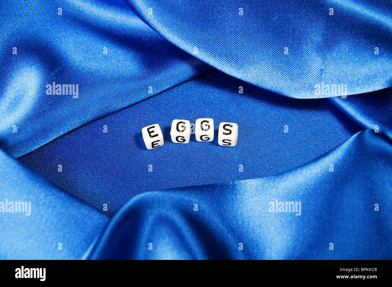 Royal blue satin background with rich folds and wrinkles for texture is the word eggs in black and white cube lettering series Stock Photo