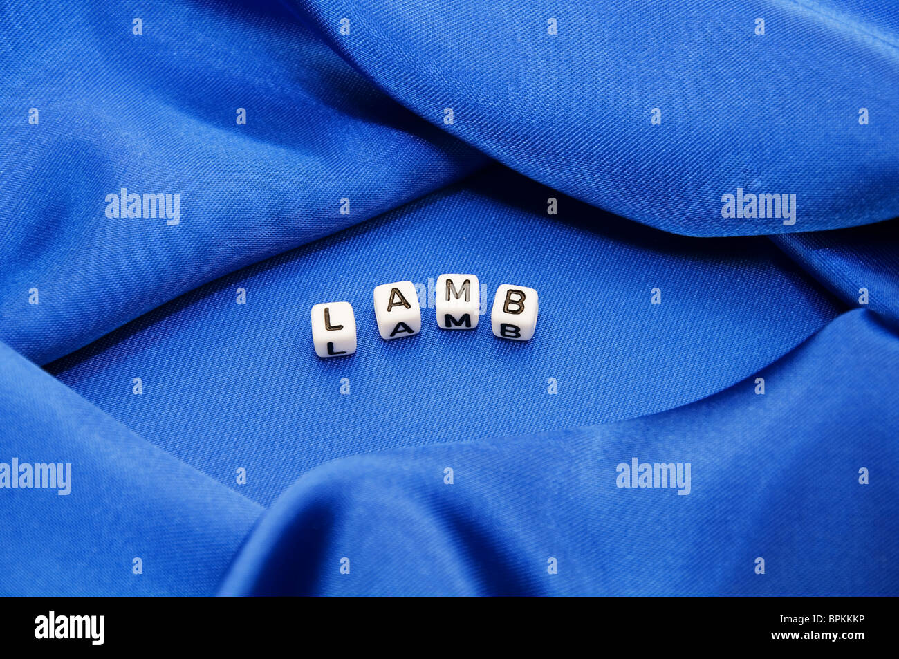 Royal blue satin background with rich folds and wrinkles for texture is the word lamb in black and white cube lettering series Stock Photo