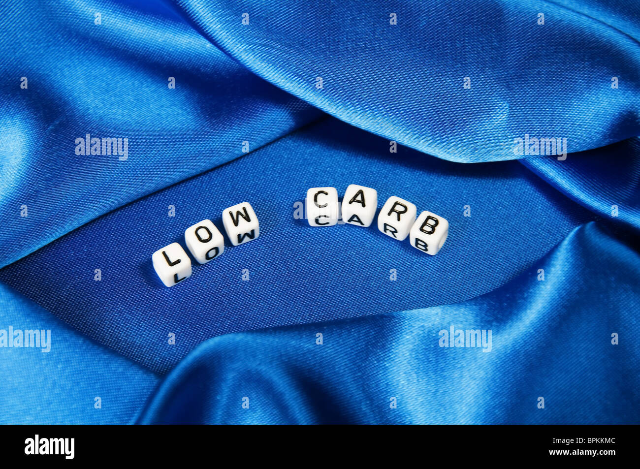 Royal blue satin background with rich folds and wrinkles for texture is the word low carb in cube lettering in series Stock Photo