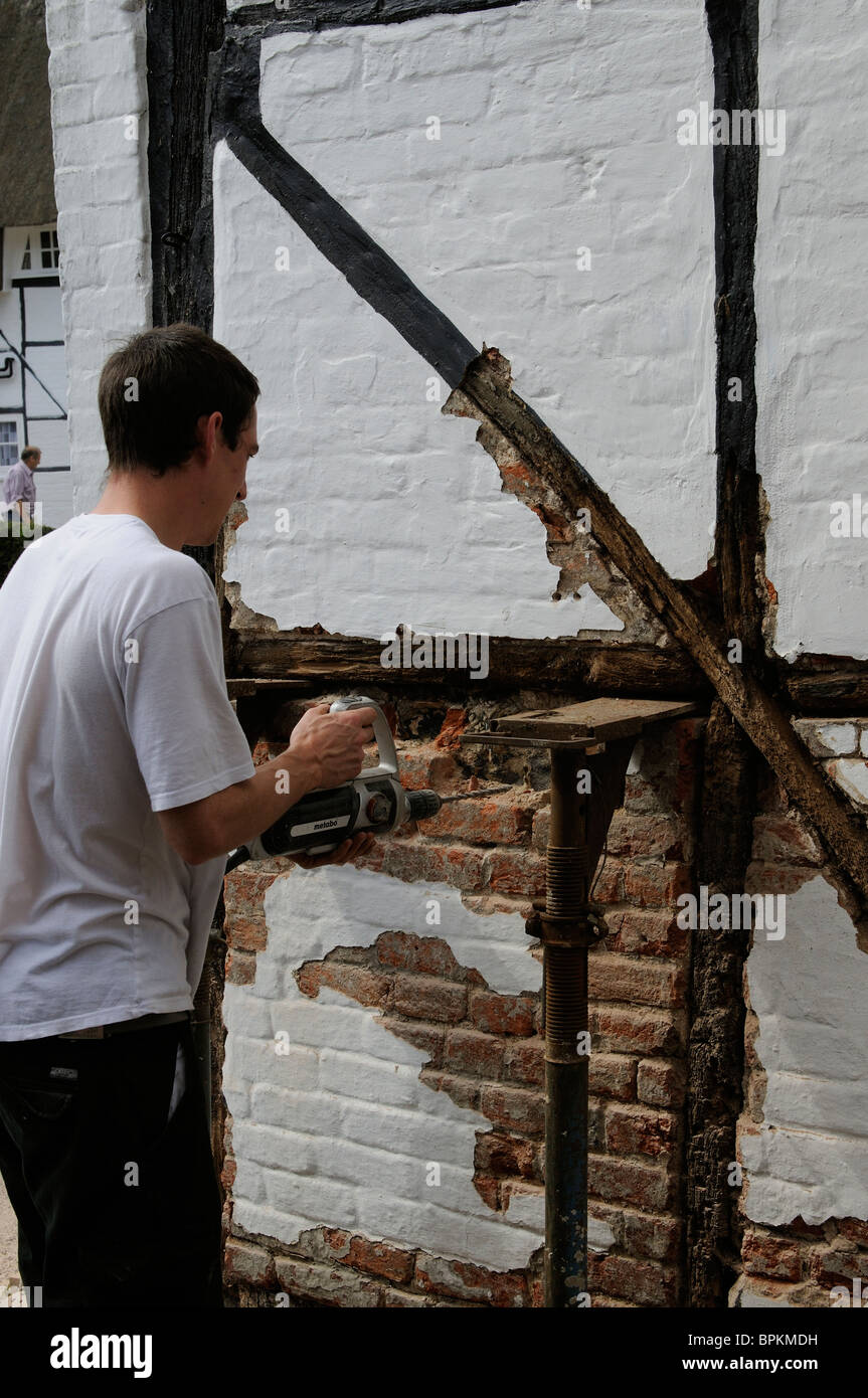 Renovating an old timber framed listed building Workman removing bricks & rendering before the installation of new oak beams Stock Photo