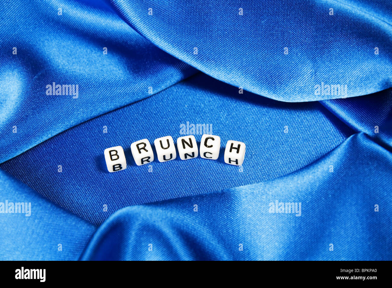Royal blue satin background with rich folds and wrinkles for texture is the word brunch in black and white cube lettering series Stock Photo